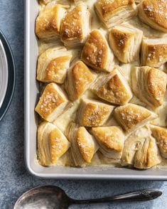 a baking dish filled with baked goods on top of a blue countertop next to two bowls and spoons