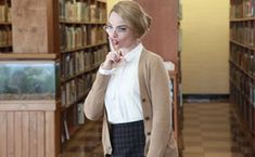 a woman standing in a library looking at the camera and making a funny face with her hand