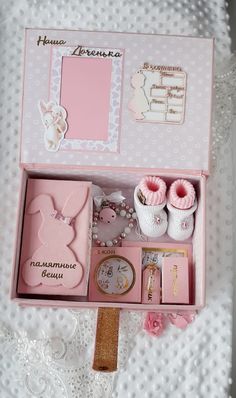 a pink box filled with baby items on top of a white bed covered in lace