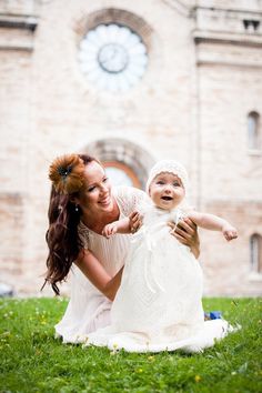 a woman holding a baby in front of a building with a clock on the wall