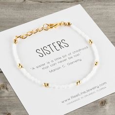 a white beaded bracelet with gold beads on it, sitting next to a card