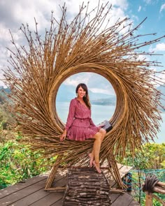 a woman sitting on top of a wooden chair made out of sticks and branches with a lake in the background