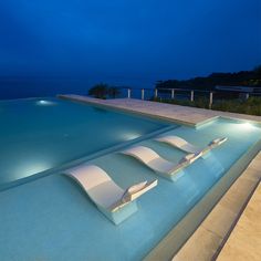 an empty swimming pool at night with lounge chairs on the edge and water in the background