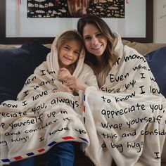 two women wrapped up in blankets with words written on them and one woman smiling at the camera