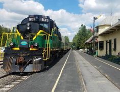 a green and yellow train traveling down tracks next to a white building with a flag on it