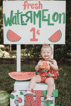 a baby sitting on top of a watermelon sign