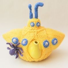 a knitted yellow tea pot with blue flowers on the bottom and an odd shaped object in the middle