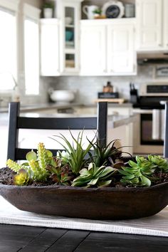 a bowl filled with succulents on top of a wooden table next to a kitchen