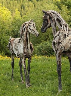 two wooden horses standing next to each other on a lush green field