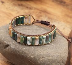 Discover the perfect blend of earthy elegance and timeless craftsmanship with our Bohemian Tube Beads Natural Stone Leather Wrap Bracelet. Handcrafted with care, this unisex piece features 4x13mm tube-shaped natural stone beads, each with its own unique hue and texture, making every bracelet a one-of-a-kind treasure. The genuine leather cord offers durability and a touch of rugged sophistication, while the antique-finished zinc alloy button adds a vintage charm. The adjustable design ensures a perfect fit for any wrist size, making it a versatile accessory for both men and women. Please note that due to the natural variations in gemstones, each bracelet will have its own distinct color and shape. Embrace the individuality of your piece and celebrate its uniqueness--just like you. Elevate y Adjustable Moss Agate Beaded Jewelry, Brown Agate Beaded Bracelet With Gemstones, Earthy Beaded Bracelets With Natural Agate Stones, Adjustable Beaded Jasper Bracelets, Adjustable Jasper Beaded Bracelets, Earthy Agate Beaded Bracelets With Natural Stones, Adjustable Jasper Bracelets With Natural Stones, Adjustable Agate Cuff Bracelet For Gifts, Brown Agate Gemstone Beaded Bracelet