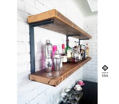 a wooden shelf filled with lots of bottles on top of a white brick wall next to cups and glasses