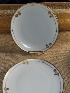 two white and gold plates sitting next to each other on top of a brown cloth