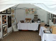 a white tent with pictures on the wall and tables under it in front of them