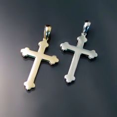 two cross pendants sitting on top of a black surface, one is white and the other is gold