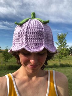 a woman wearing a purple crocheted hat with a green leaf on the top