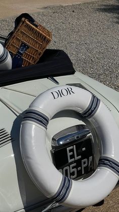 an old white car with a life preserver on the hood and seat cover is parked next to a wicker basket