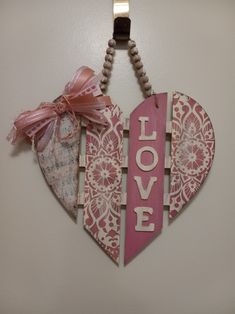 a wooden heart hanging on a wall with the word love spelled in white and pink