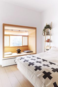 a bed sitting under a window next to a wooden shelf filled with pots and vases