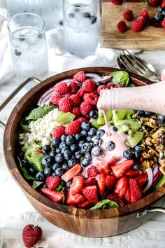 a person pouring dressing into a bowl filled with fresh berries and other fruits, including raspberries