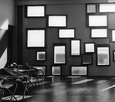 black and white photograph of chairs in front of a wall with many pictures on it