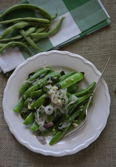 a white plate topped with green beans and onions next to a fork on a table