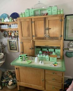 an old fashioned kitchen with lots of green items on the counter and cabinets above it