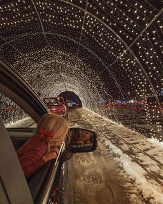 a woman driving down a snow covered road in a tunnel with lights on the ceiling