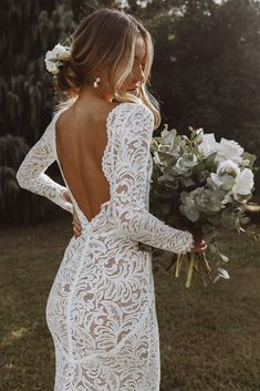 a woman in a white lace dress holding a bouquet of flowers and looking at her back