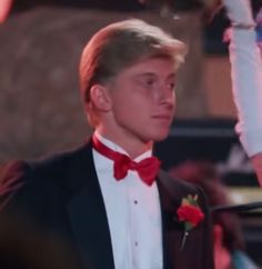 a young man in a tuxedo and red bow tie standing next to a microphone