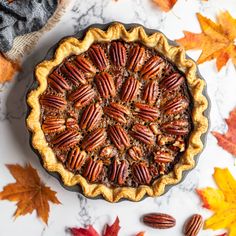 a pecan pie on a marble table surrounded by autumn leaves