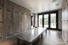 an empty room with wooden cabinets and a long table in the center, surrounded by glass doors