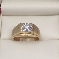 a gold ring with a princess cut diamond in it's center, sitting inside a white box