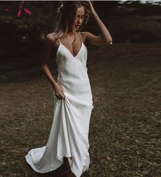 a woman in a white dress is standing on the grass with her hands behind her head