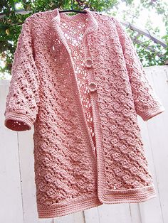 a pink crocheted cardigan hanging on a clothes line with trees in the background