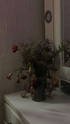 a vase filled with flowers sitting on top of a white dresser next to a mirror