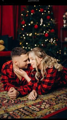 a man and woman laying on the floor in front of a christmas tree