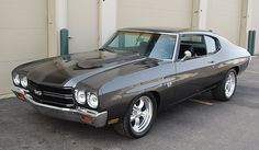 an old muscle car parked in front of a garage