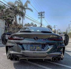 the rear end of a black sports car parked in a parking lot with palm trees