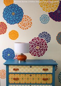 a dresser with a lamp on top of it in front of a colorful wallpaper