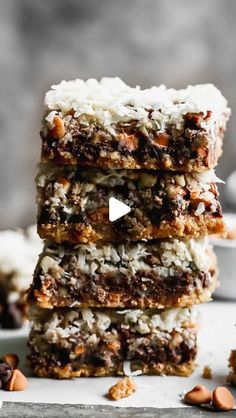 three pieces of chocolate coconut bars stacked on top of each other with nuts scattered around them