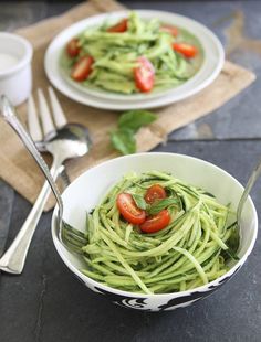 a white bowl filled with green pasta and tomatoes