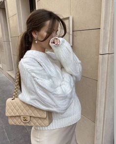 a woman is leaning against a wall with her hand on her shoulder and wearing a white sweater