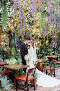 a bride and groom standing in front of a table with flowers hanging from the ceiling