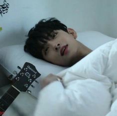 a young man laying in bed with his head on the pillow while holding an acoustic guitar