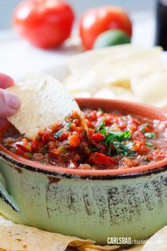 someone dipping tortilla chips into a bowl of salsa