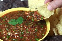 a hand dipping a tortilla chip into a bowl of chili