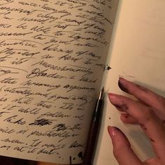 a hand holding a pen over a book with writing on the pages in cursive ink