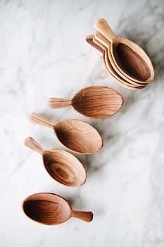 four wooden spoons lined up on a white marble counter top with one being used as a serving utensil