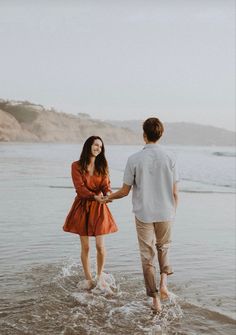 a man and woman are walking in the water at the beach holding each other's hands