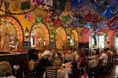 people sitting at tables in a brightly lit restaurant with colorful lights hanging from the ceiling